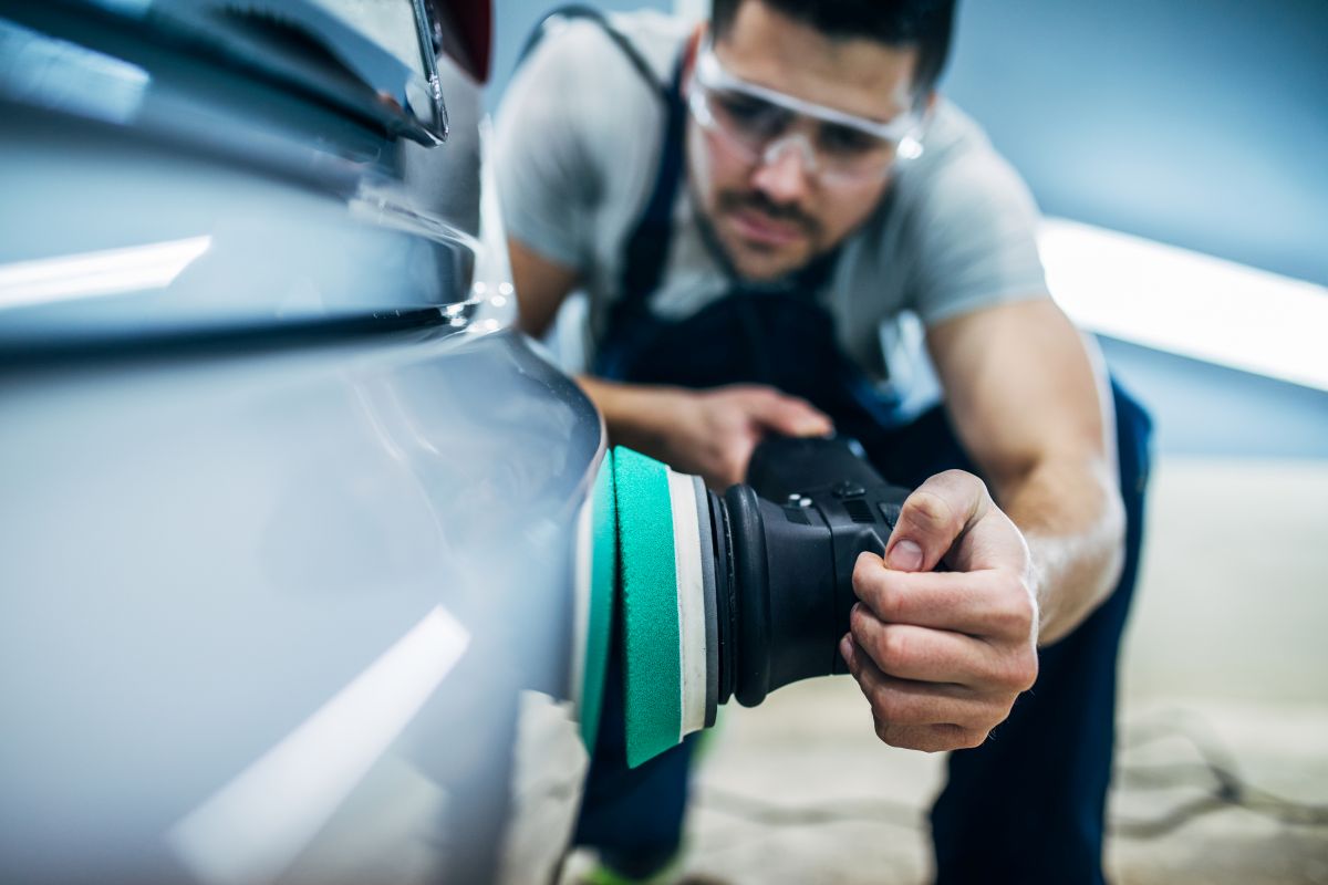 Close up photo of man hand in black protective gloves cleaning radiator grille in foam with special brush. Carwash and detailing. Washing machine at the station. Car washing concept